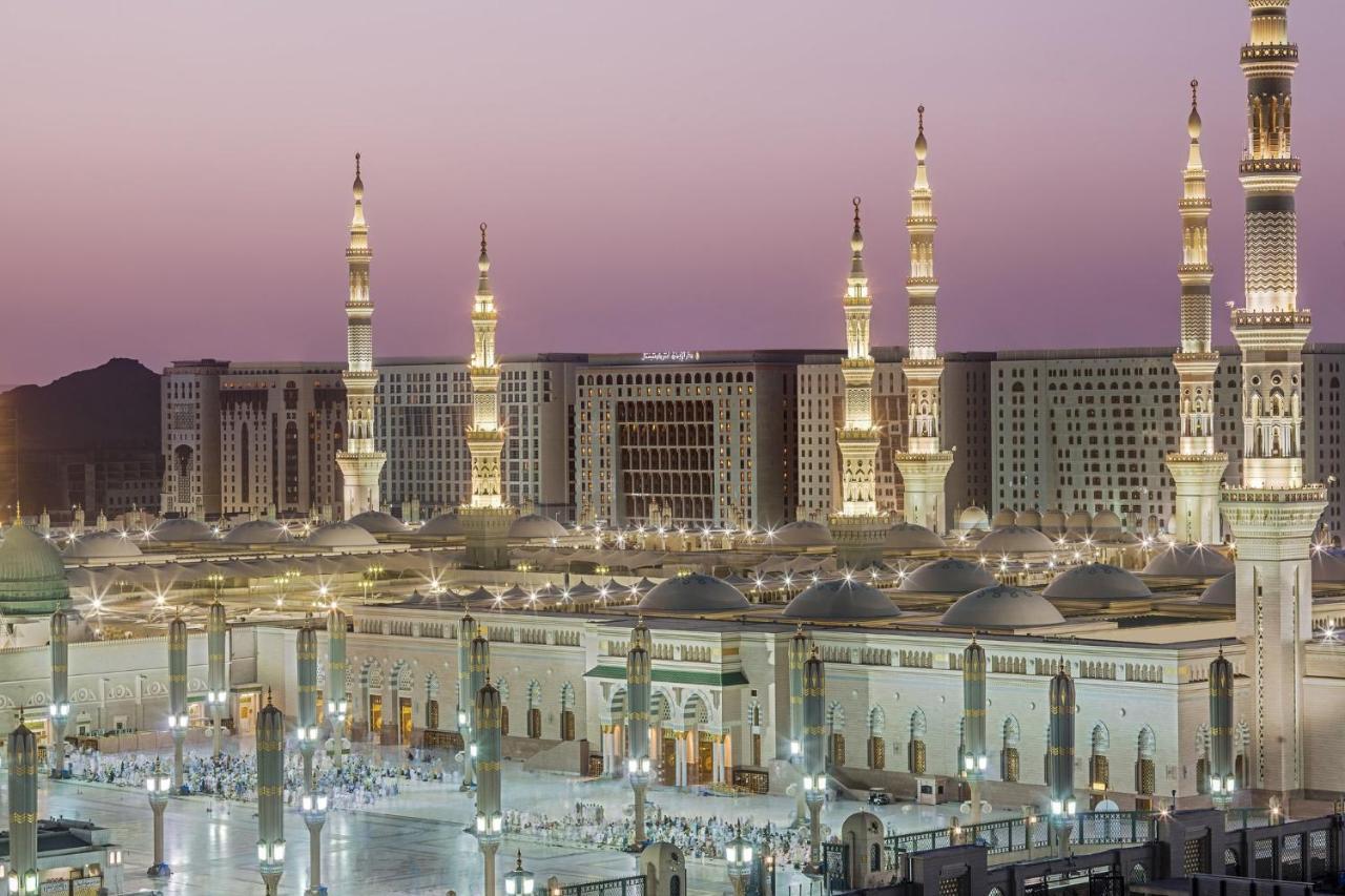 Intercontinental Dar Al Iman Madinah By Ihg Ξενοδοχείο Μεδίνα Εξωτερικό φωτογραφία The photo shows a view of an expansive mosque complex, featuring several tall minarets that are illuminated against a twilight sky. The structure appears grand and is likely adorned with intricate architectural details. There are people gathered in t