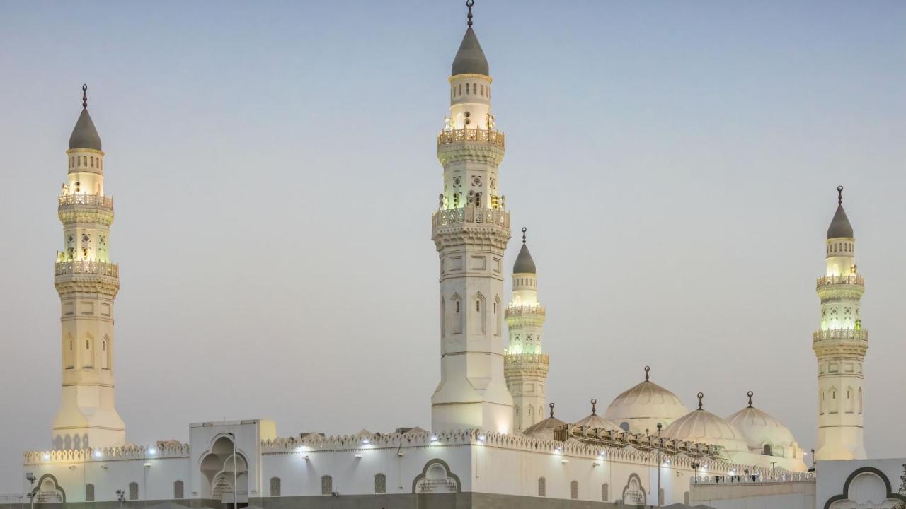 Intercontinental Dar Al Iman Madinah By Ihg Ξενοδοχείο Μεδίνα Εξωτερικό φωτογραφία The image shows a mosque with distinct architectural features, including tall minarets and domes. The minarets are highlighted, likely lit up in the evening, showcasing intricate design elements typical of Islamic architecture. The overall scene conv