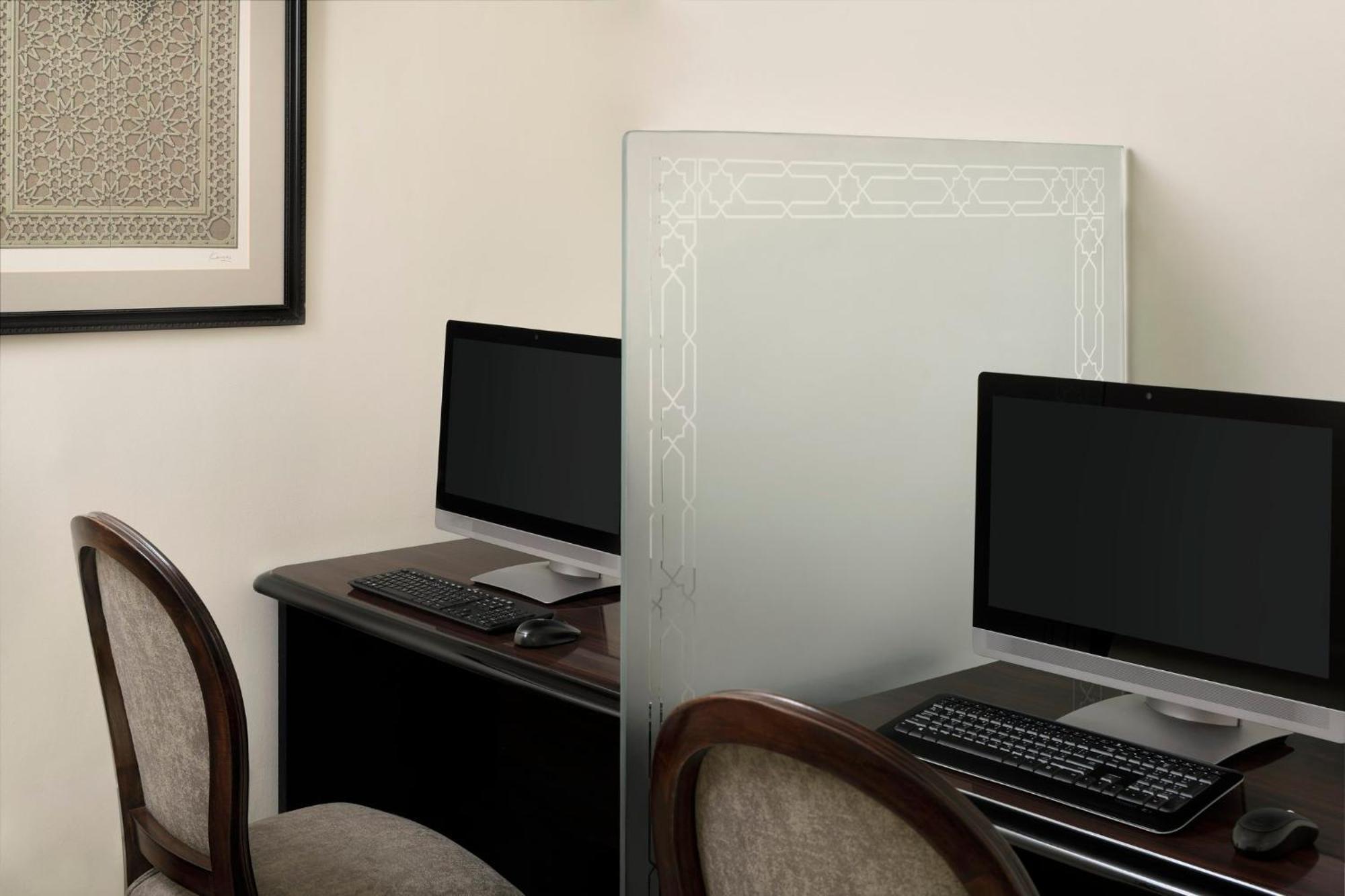Intercontinental Dar Al Iman Madinah By Ihg Ξενοδοχείο Μεδίνα Εξωτερικό φωτογραφία The photo shows a small office or workspace area featuring two computer stations. Each station has a black monitor, a keyboard, and appears to be set up on a dark wooden desk. A translucent glass partition is placed between the two workstations, prov