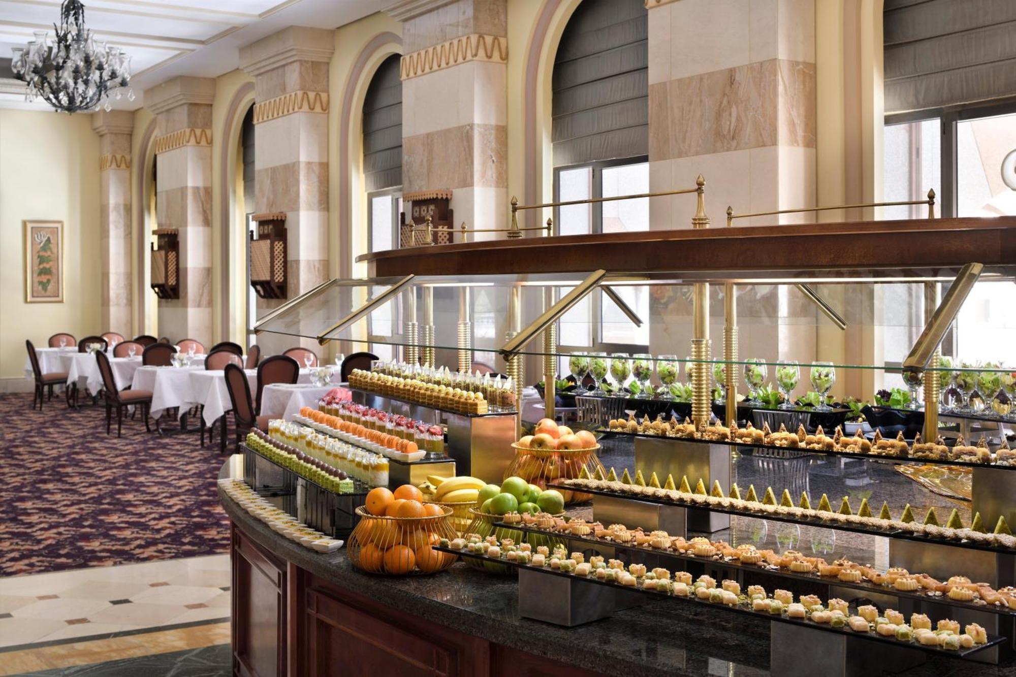 Intercontinental Dar Al Iman Madinah By Ihg Ξενοδοχείο Μεδίνα Εξωτερικό φωτογραφία The photo depicts an elegant dining area featuring a buffet-style display. In the foreground, a beautifully arranged buffet counter showcases an array of desserts, including miniature pastries and colorful fruit. The setting has a sophisticated ambia