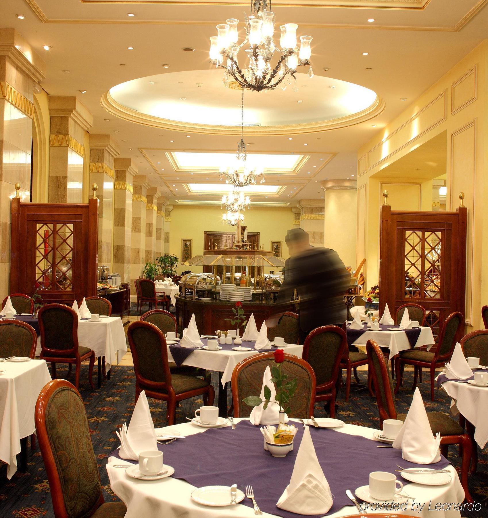 Intercontinental Dar Al Iman Madinah By Ihg Ξενοδοχείο Μεδίνα Εστιατόριο φωτογραφία The photo depicts an elegant restaurant interior. It features round tables covered with white tablecloths, each set with plates, cutlery, and folded napkins arranged into triangles. The space has a warm, inviting atmosphere with a mix of decorative e